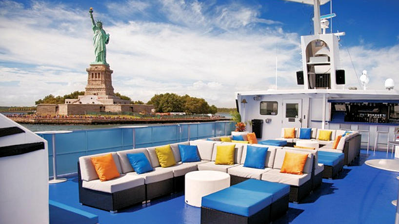 Open-air yacht deck with lounge seating and Statue of Liberty views.